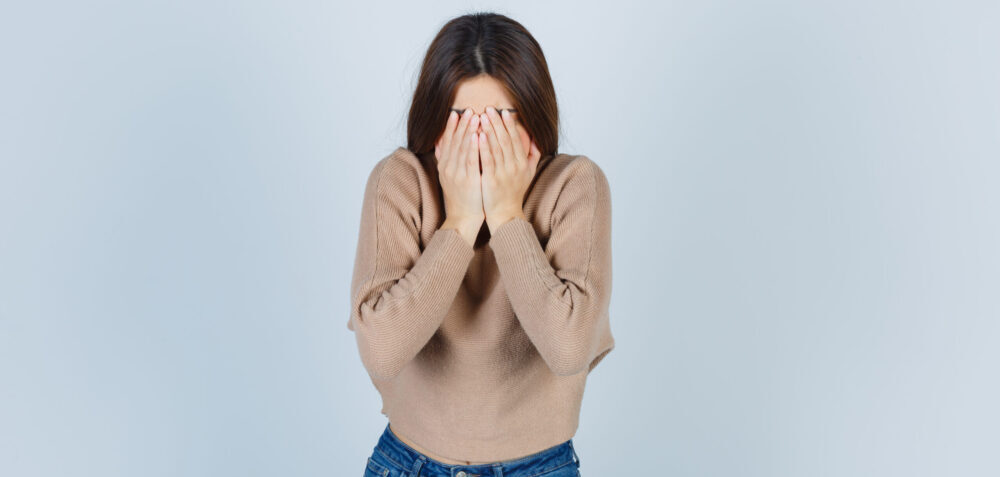 teenage girl sweater jeans covering face with hands looking depressed front view scaled e1652709666835 15